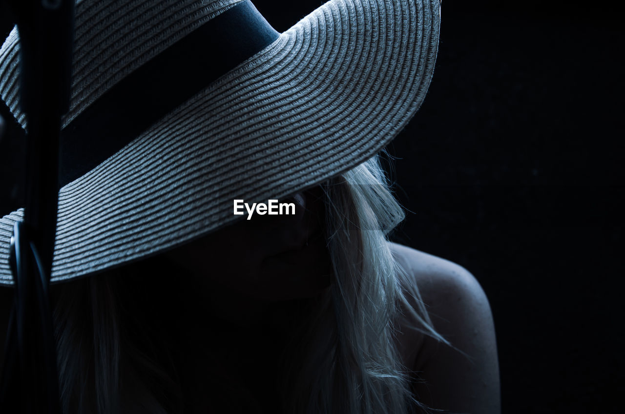 Close-up portrait of woman wearing hat against black background