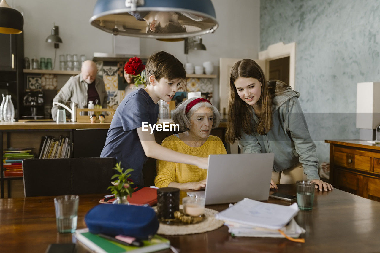 Siblings assisting grandmother using laptop on table at home