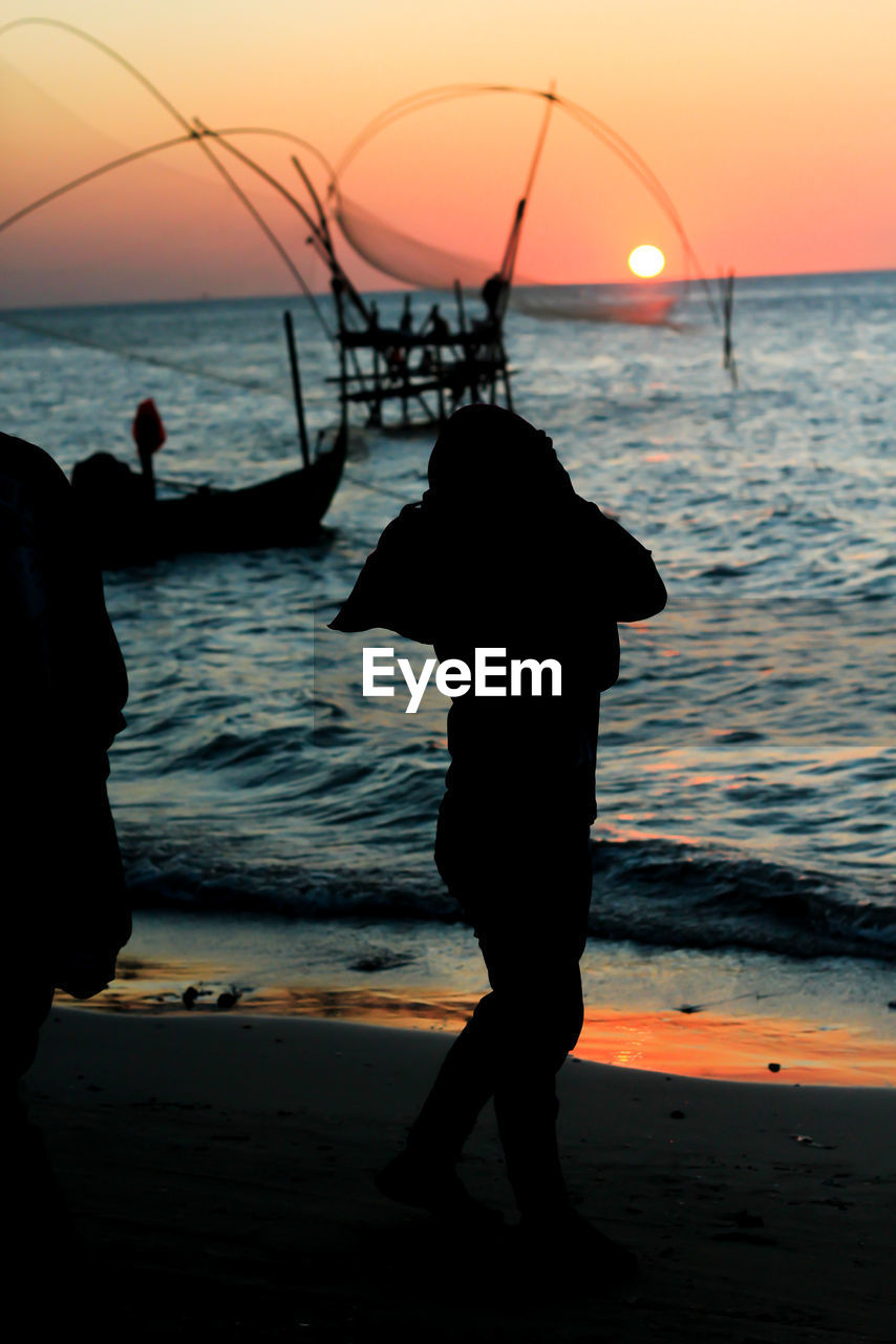 Silhouette man standing on beach against sky during sunset