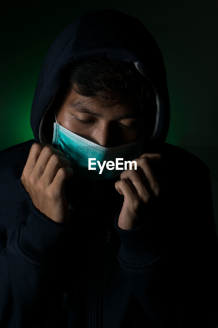 CLOSE-UP PORTRAIT OF A YOUNG MAN COVERING FACE WITH BLACK BACKGROUND