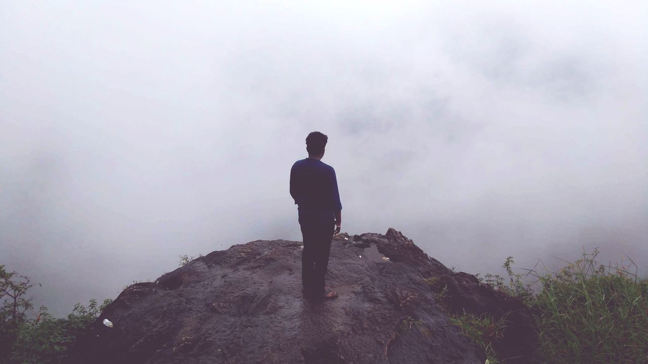 Rear view of man standing on mountain during foggy weather