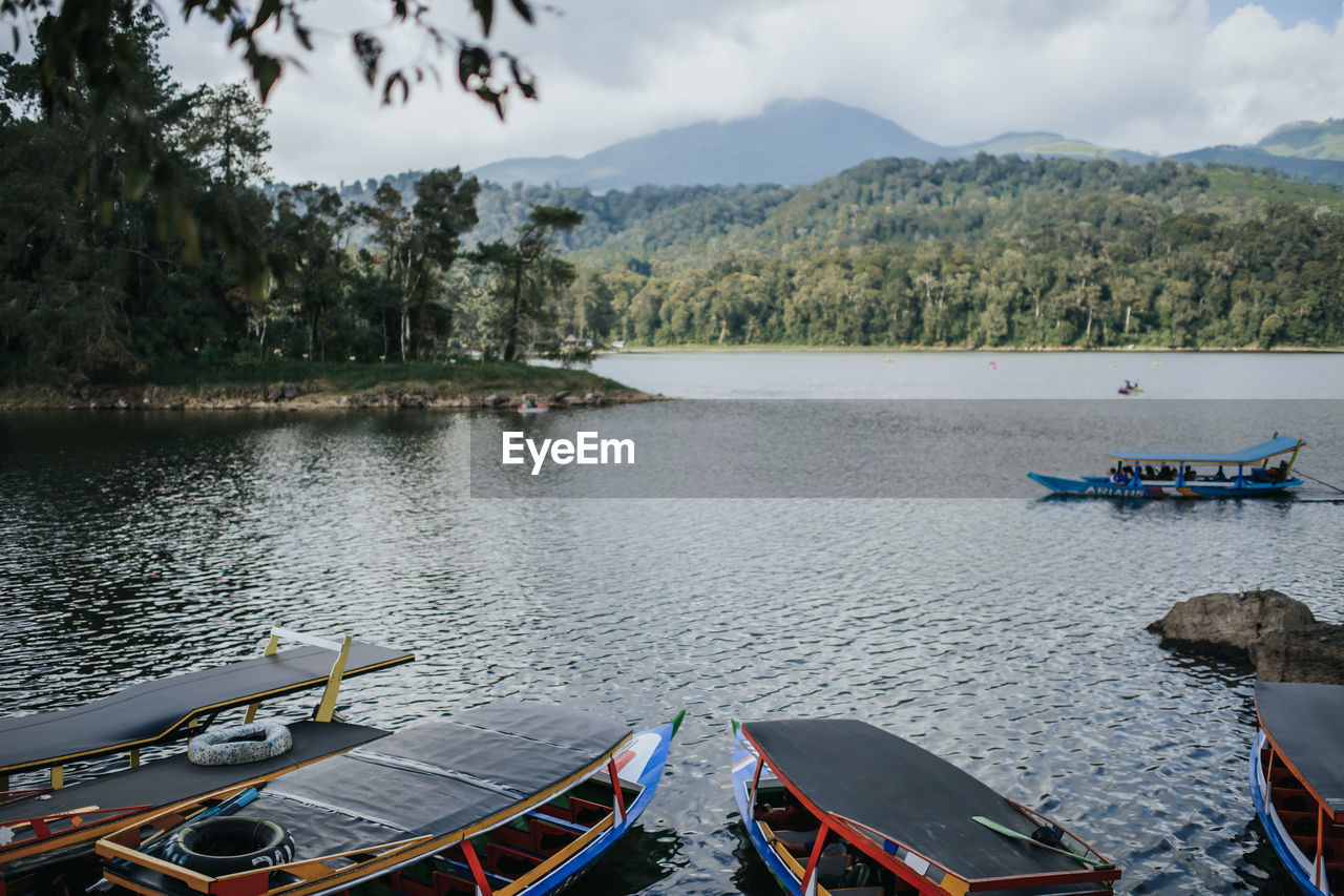 BOATS MOORED IN LAKE AGAINST SKY