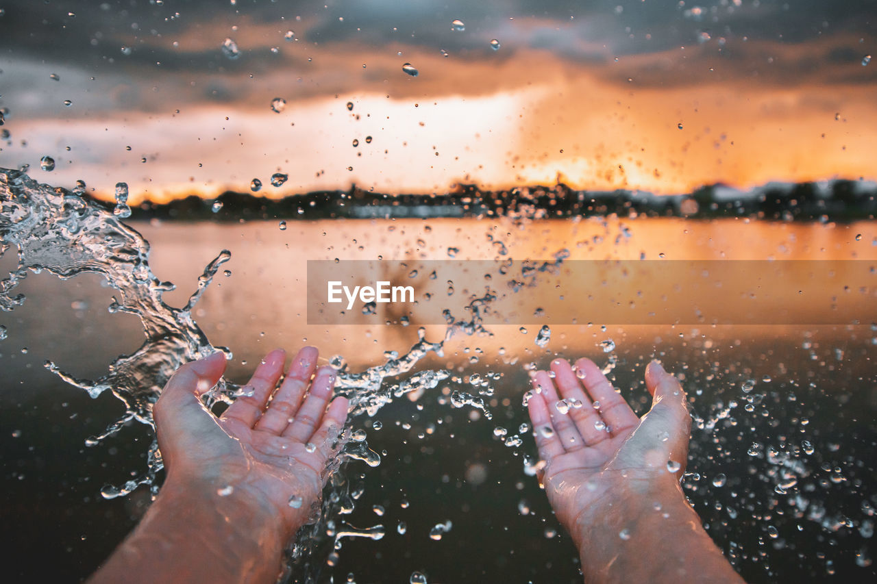 Cropped hands of person splashing water during sunset