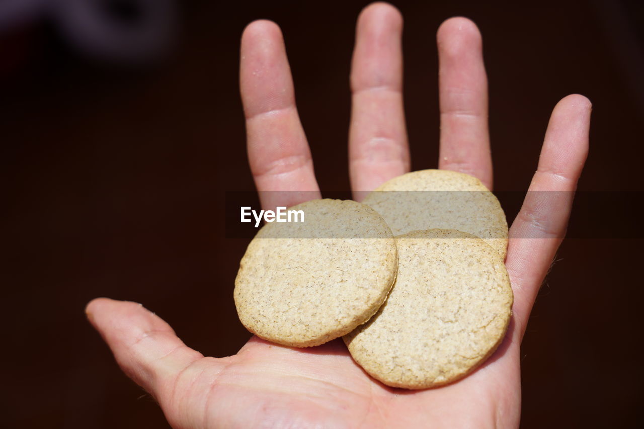 MIDSECTION OF PERSON HOLDING COOKIES AGAINST BLACK BACKGROUND