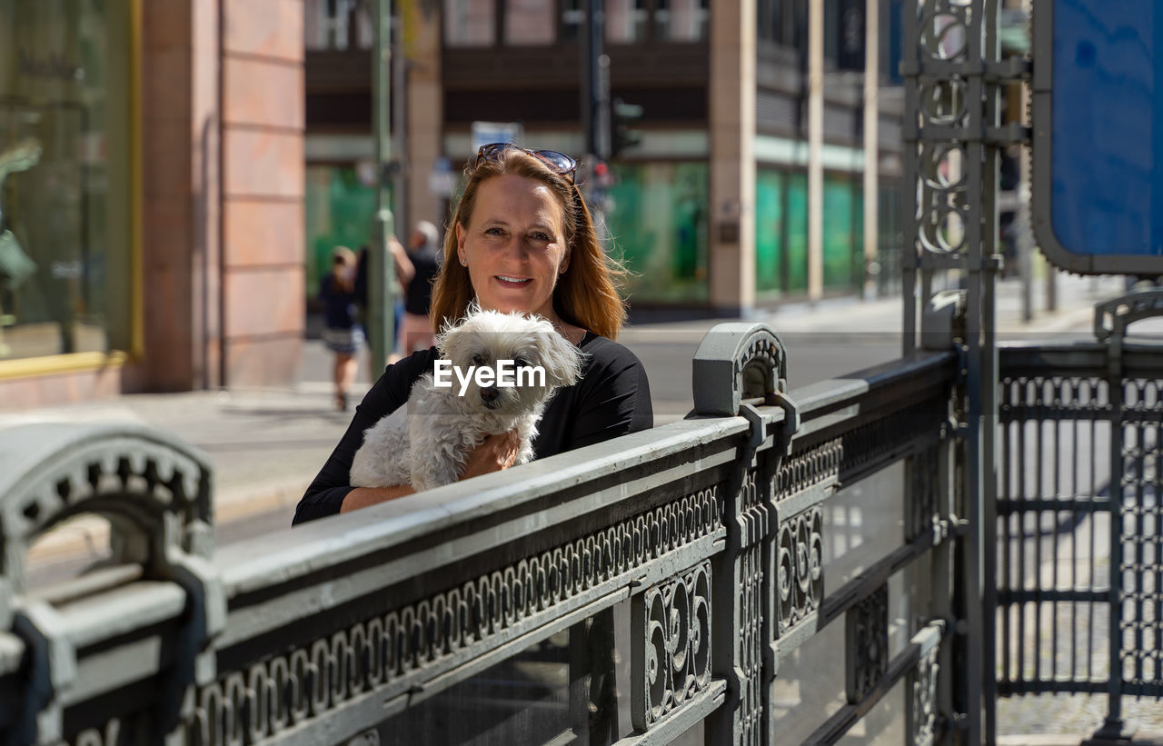 Portrait of woman with dog on railing in city