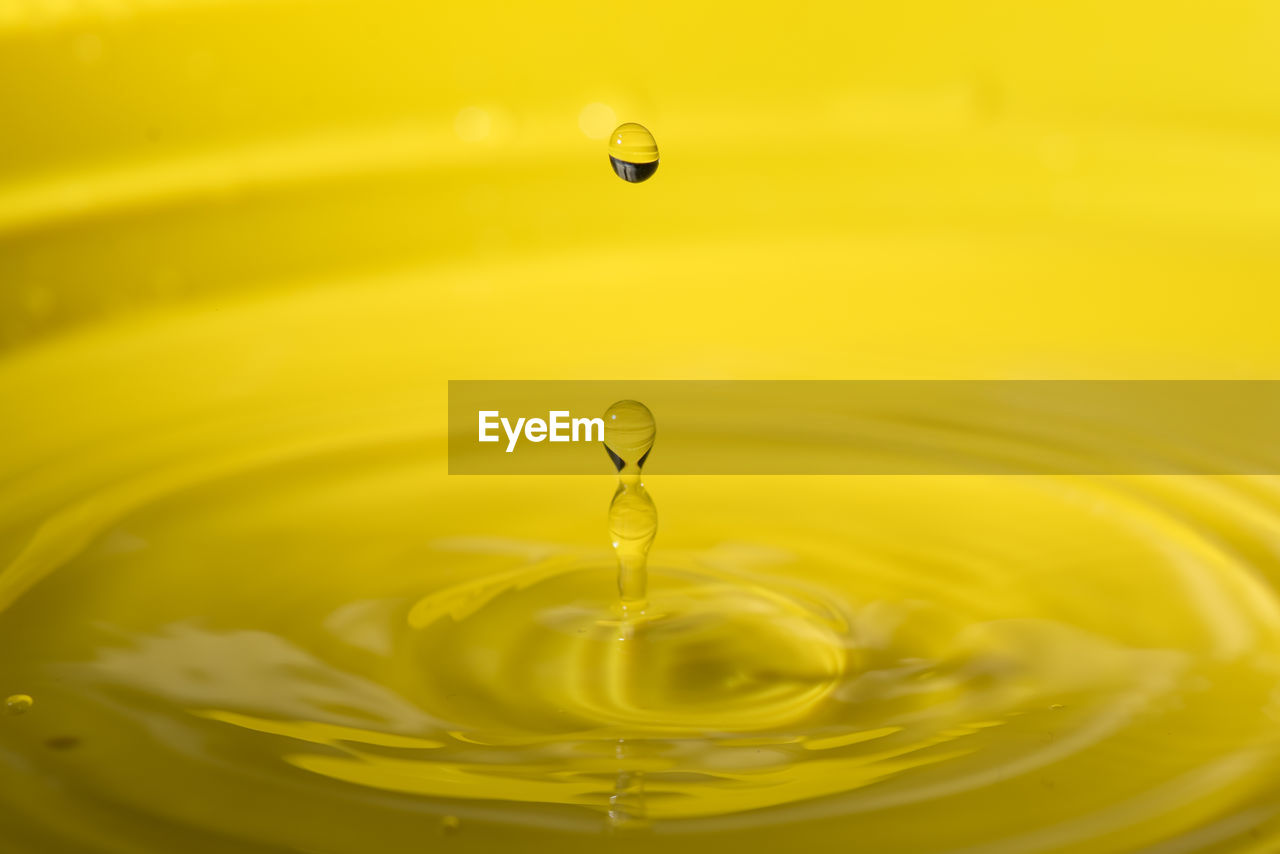 CLOSE-UP OF DROP SPLASHING IN WATER AGAINST YELLOW BACKGROUND