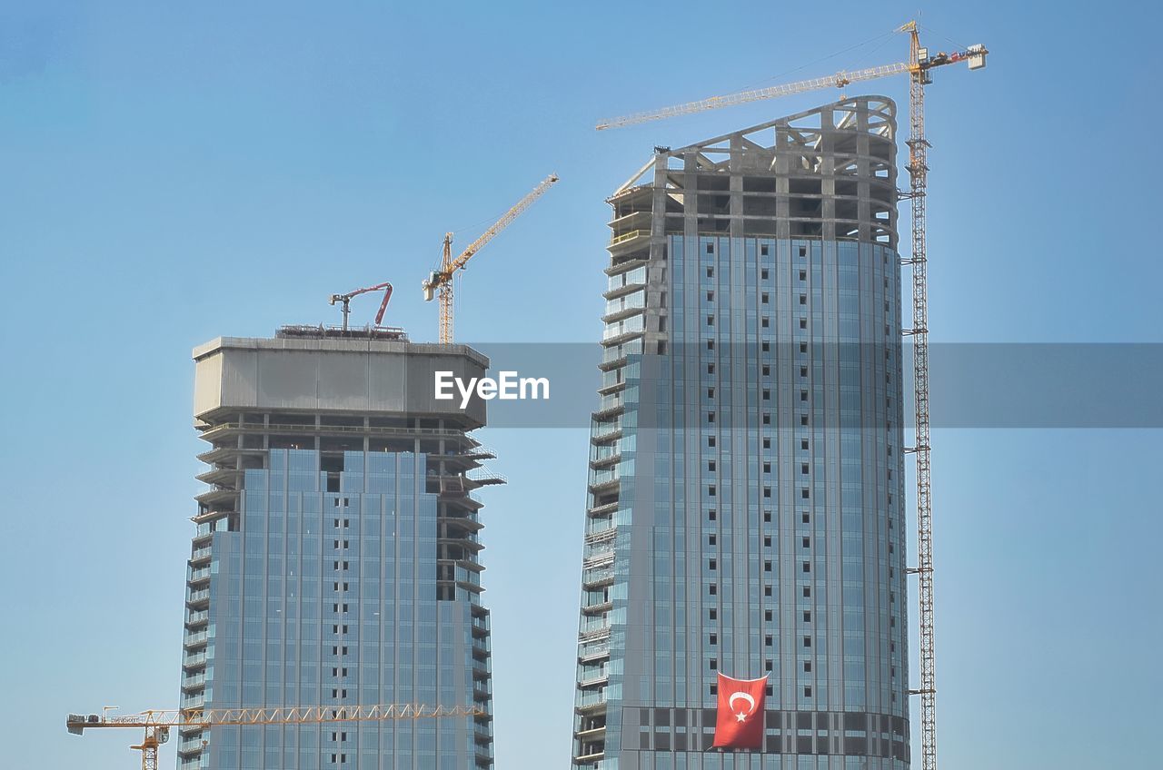 Low angle view of crane by building against clear sky