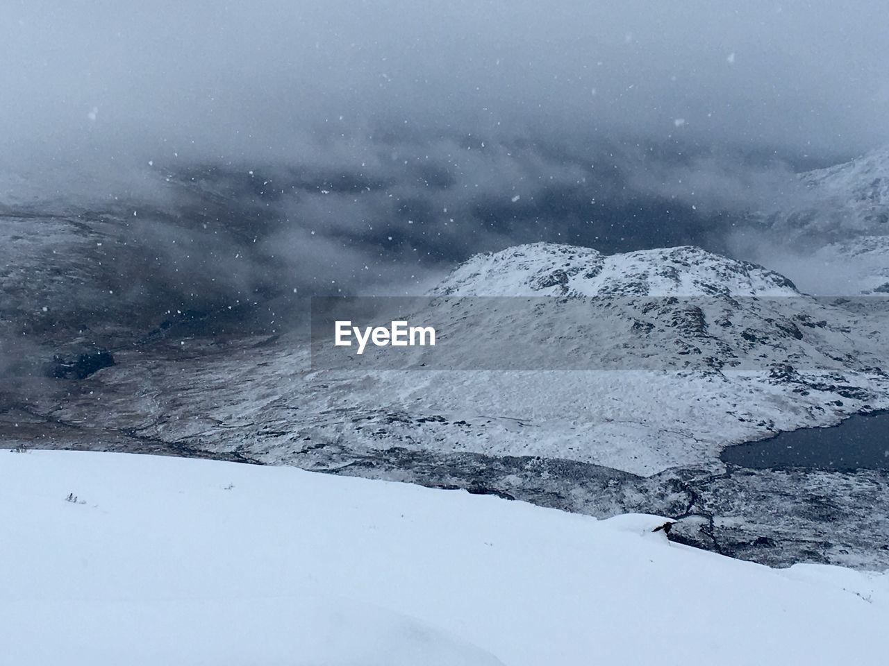 Snowcapped mountains against cloudy sky during snowfall