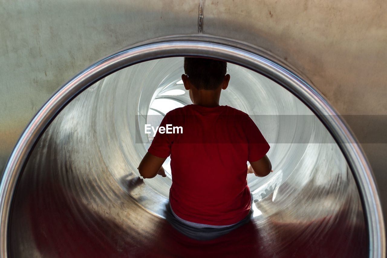 Rear view of boy sitting in slide at playground
