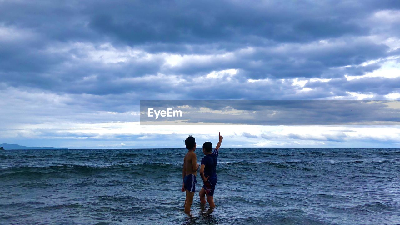 water, sea, sky, cloud, ocean, wind wave, wave, togetherness, nature, beach, horizon, horizon over water, two people, beauty in nature, leisure activity, holiday, shore, adult, land, men, trip, vacation, coast, bonding, positive emotion, women, friendship, emotion, standing, day, sports, outdoors, scenics - nature, rear view, surfing, lifestyles, full length, body of water, child, happiness, motion, young adult, water sports, enjoyment, swimming, family, travel, fun, love, summer, female, childhood