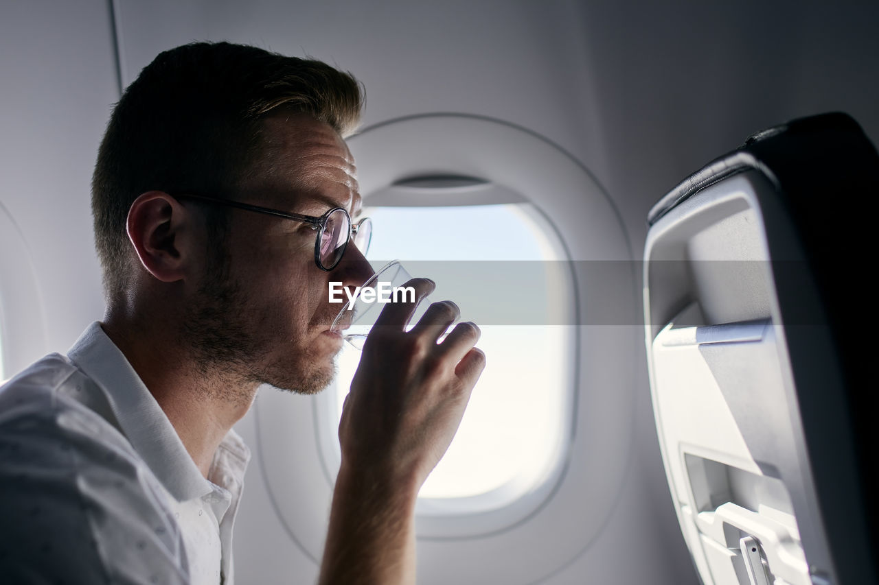 Portrait of passenger during flight. young man drinking water from plastic cup.