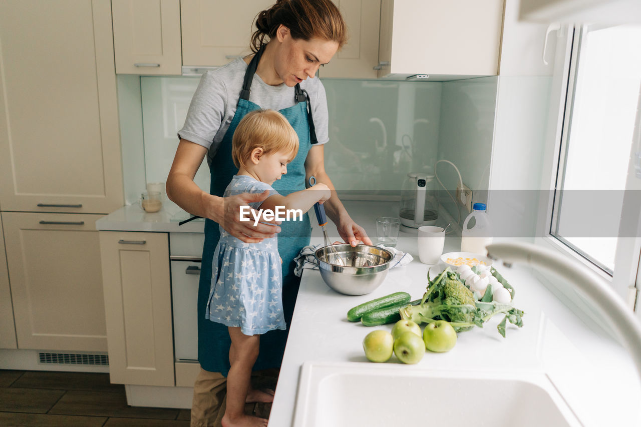 Toddler little daughter helps mom cook dinner.