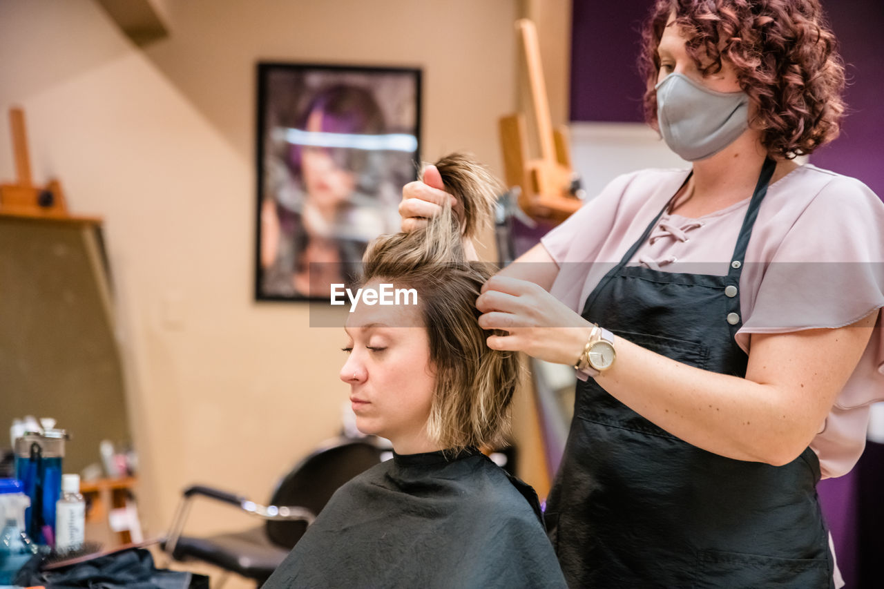 Hairdresser wearing flu mask dyeing hair of client in salon