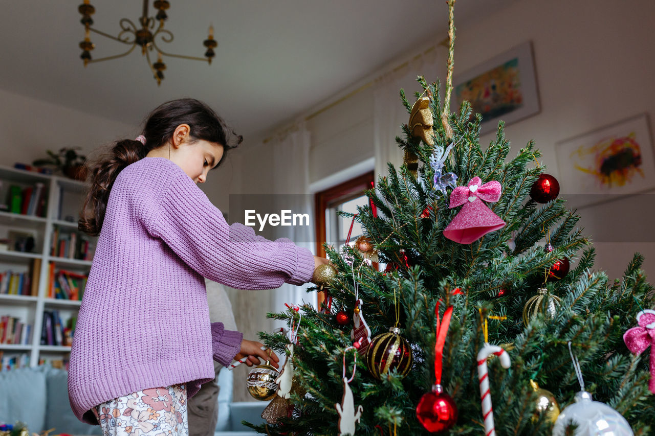 Low angle view of girl in lilac jumper decorating christmas tree at home