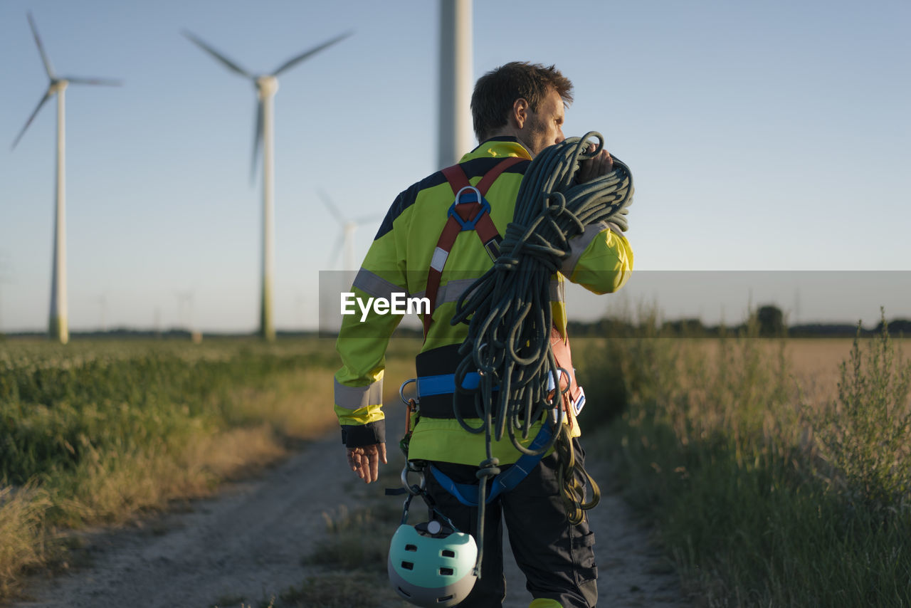 Technician walking on field path at a wind farm with climbing equipment