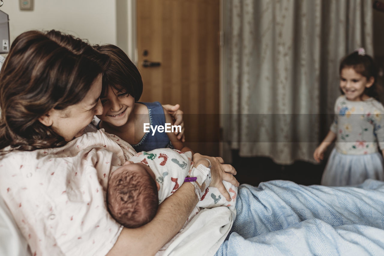Side view of mother holding newborn son meeting siblings