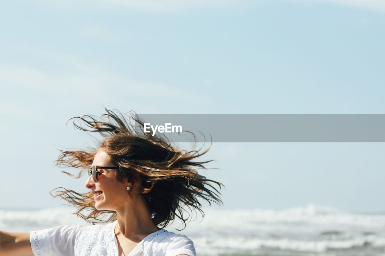 YOUNG WOMAN SMILING AGAINST SEA