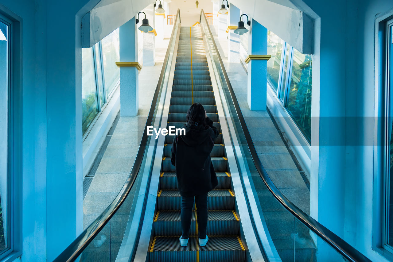 REAR VIEW OF WOMAN STANDING ON ESCALATOR IN TRAIN