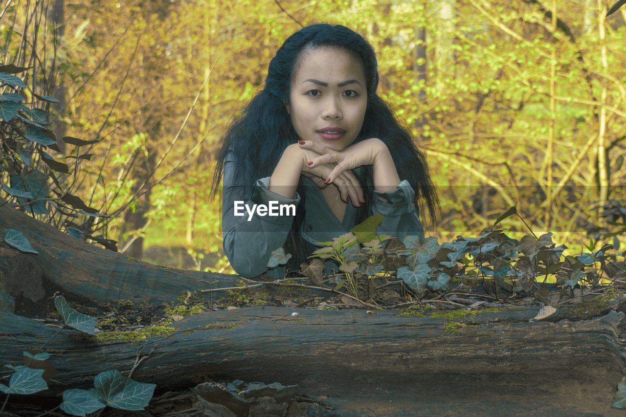 Portrait of beautiful young woman leaning on tree trunk in forest