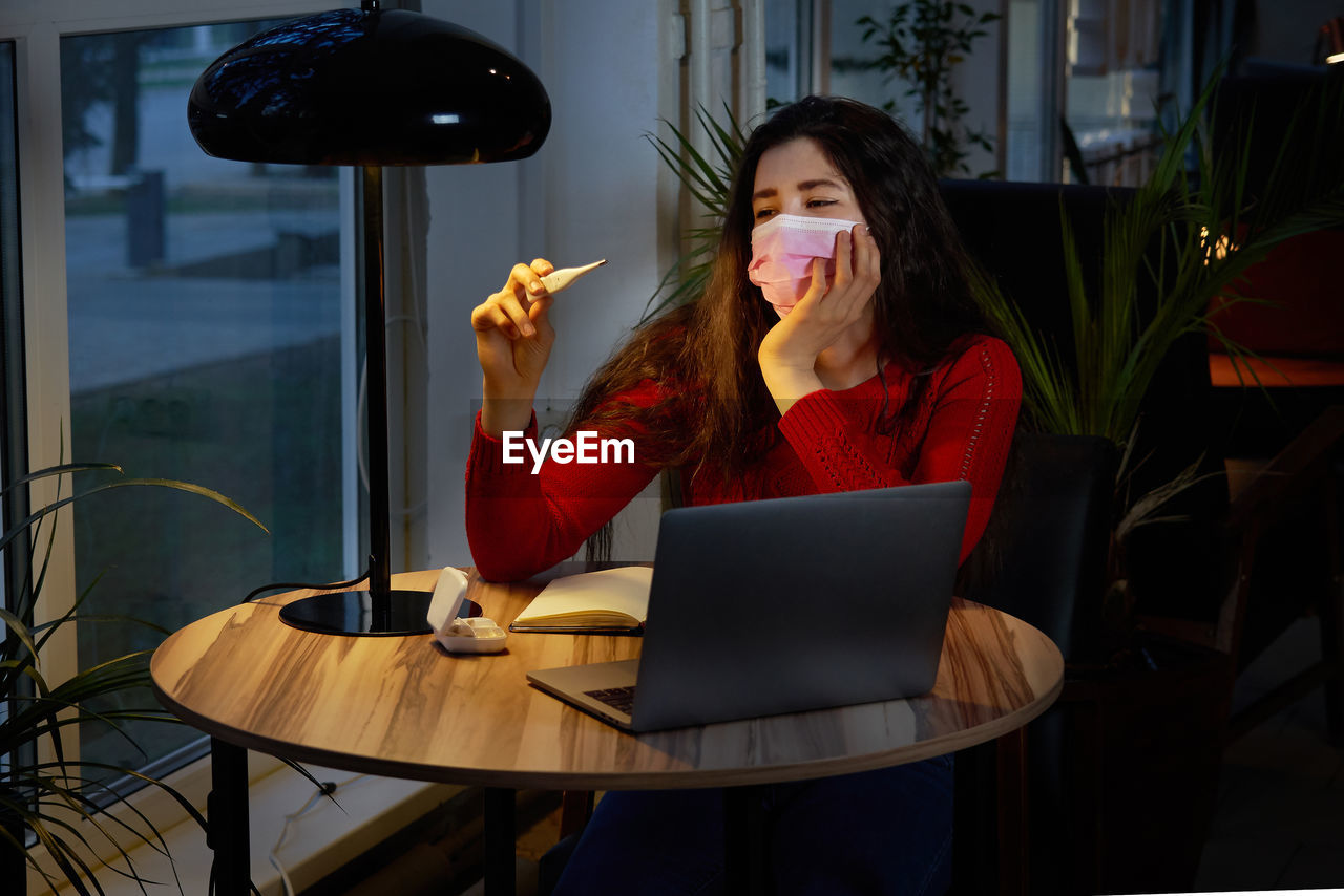 Sick woman taking temperature with thermometer