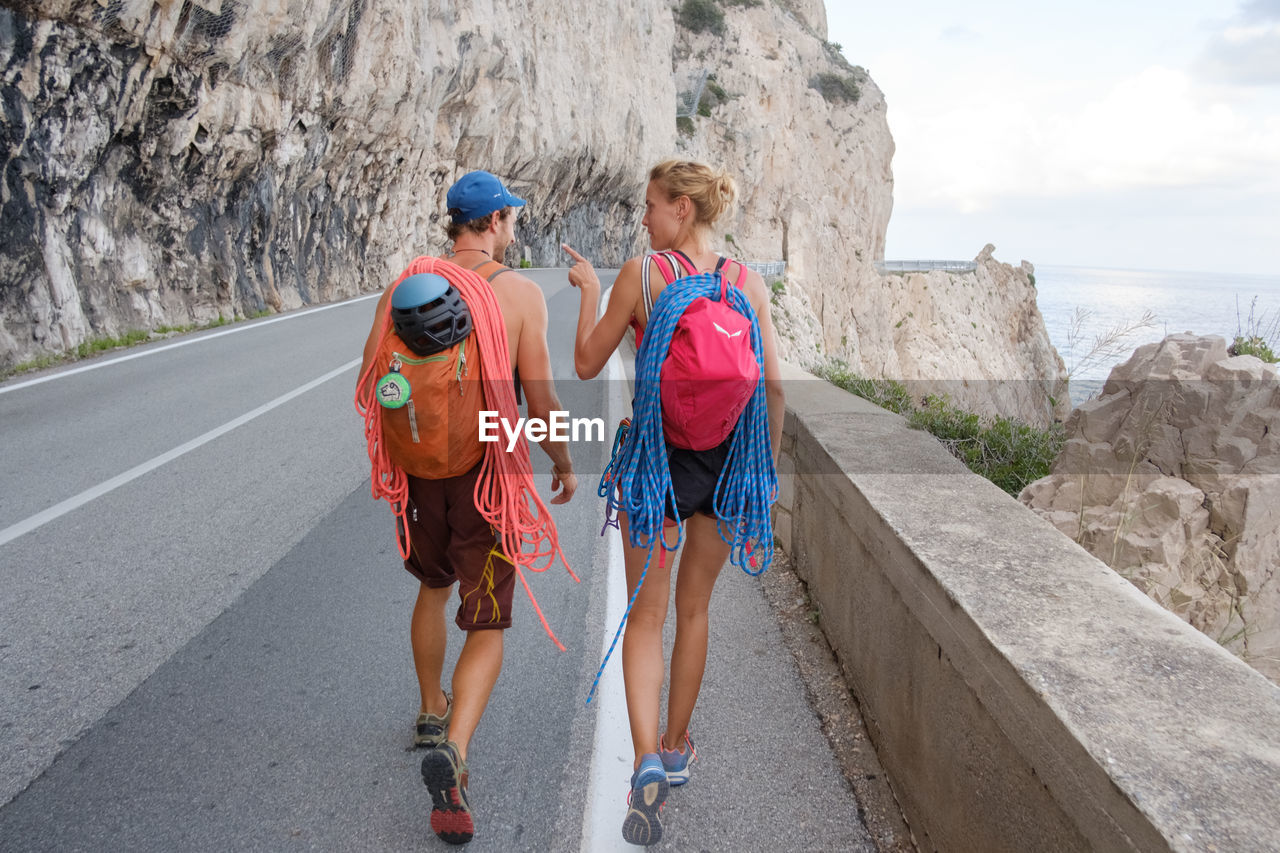 Rear view of backpackers walking on road by cliff