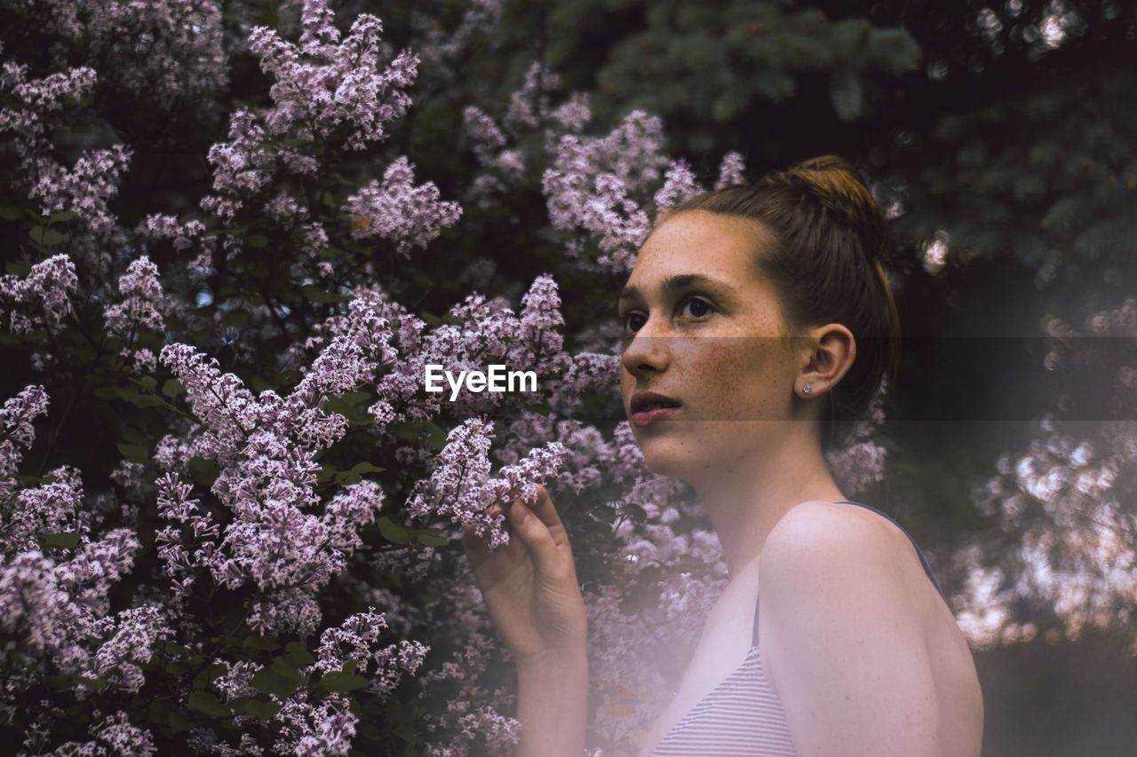 Thoughtful teenage girl looking away by flowering plants at park