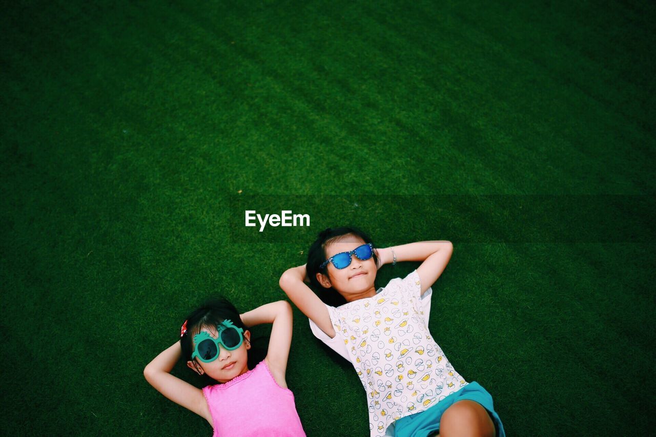 High angle view of friends wearing sunglasses lying on grassy field at park