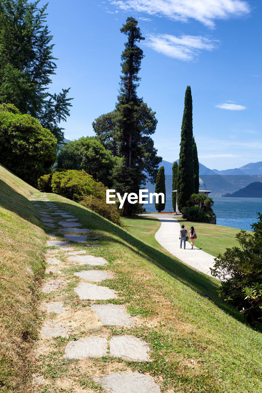 People walking on footpath by trees against sky