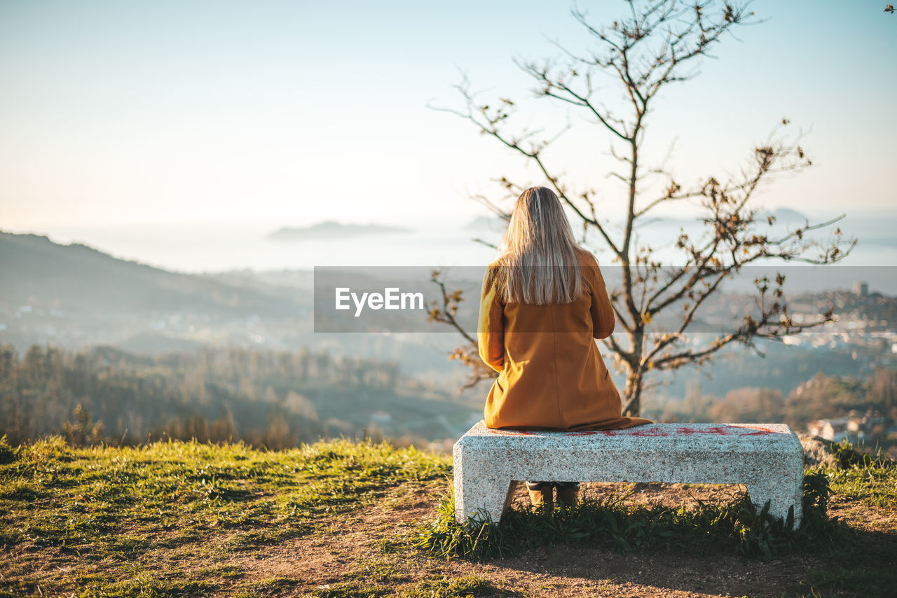 Rear view of woman sitting on bench against sky