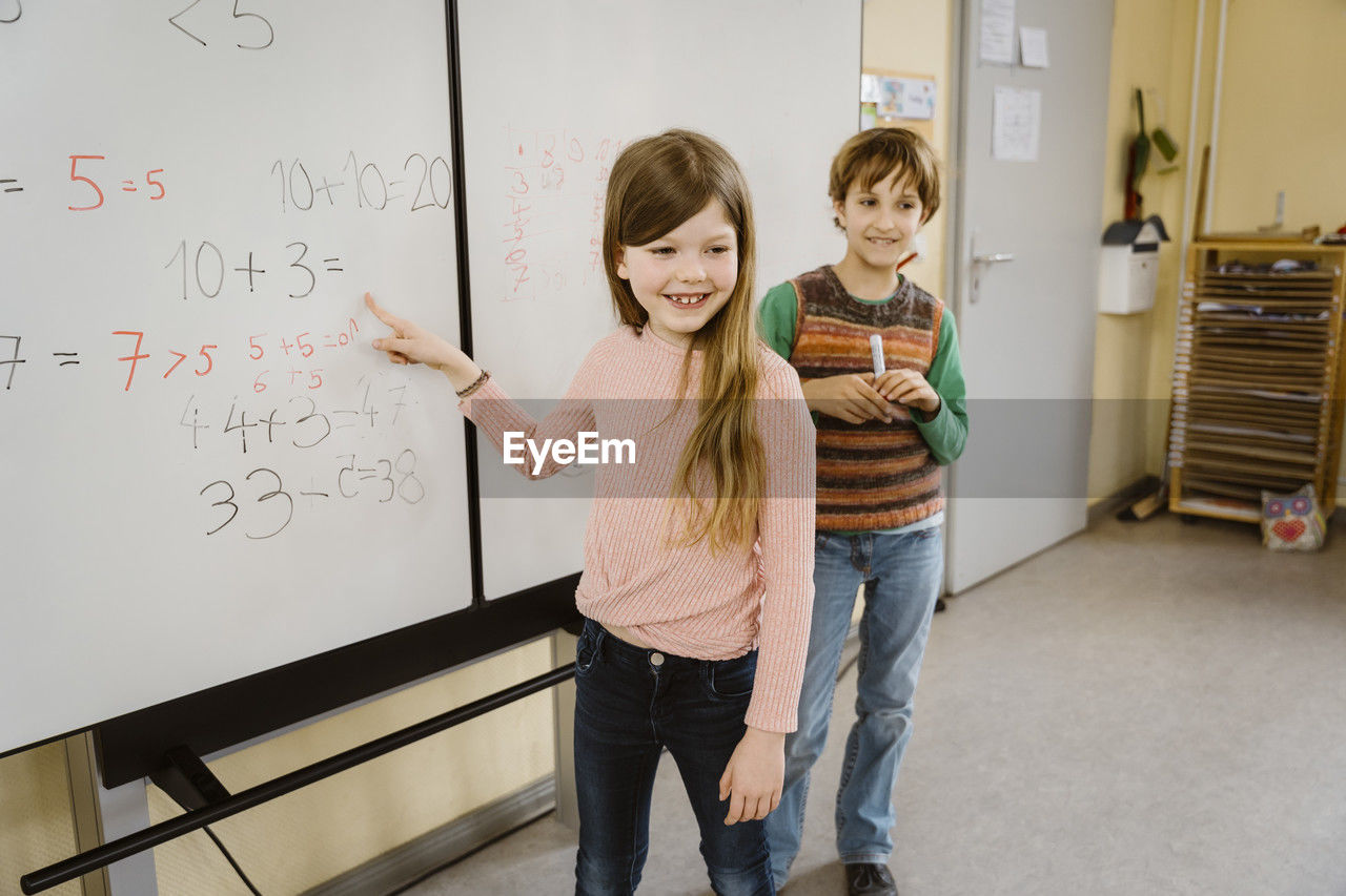 Happy girl solving maths problem with boy in classroom