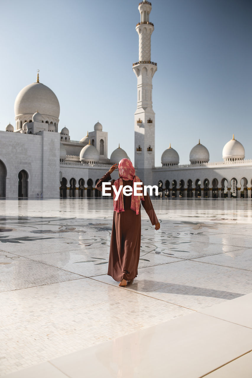 Rear view of woman walking on floor against mosque