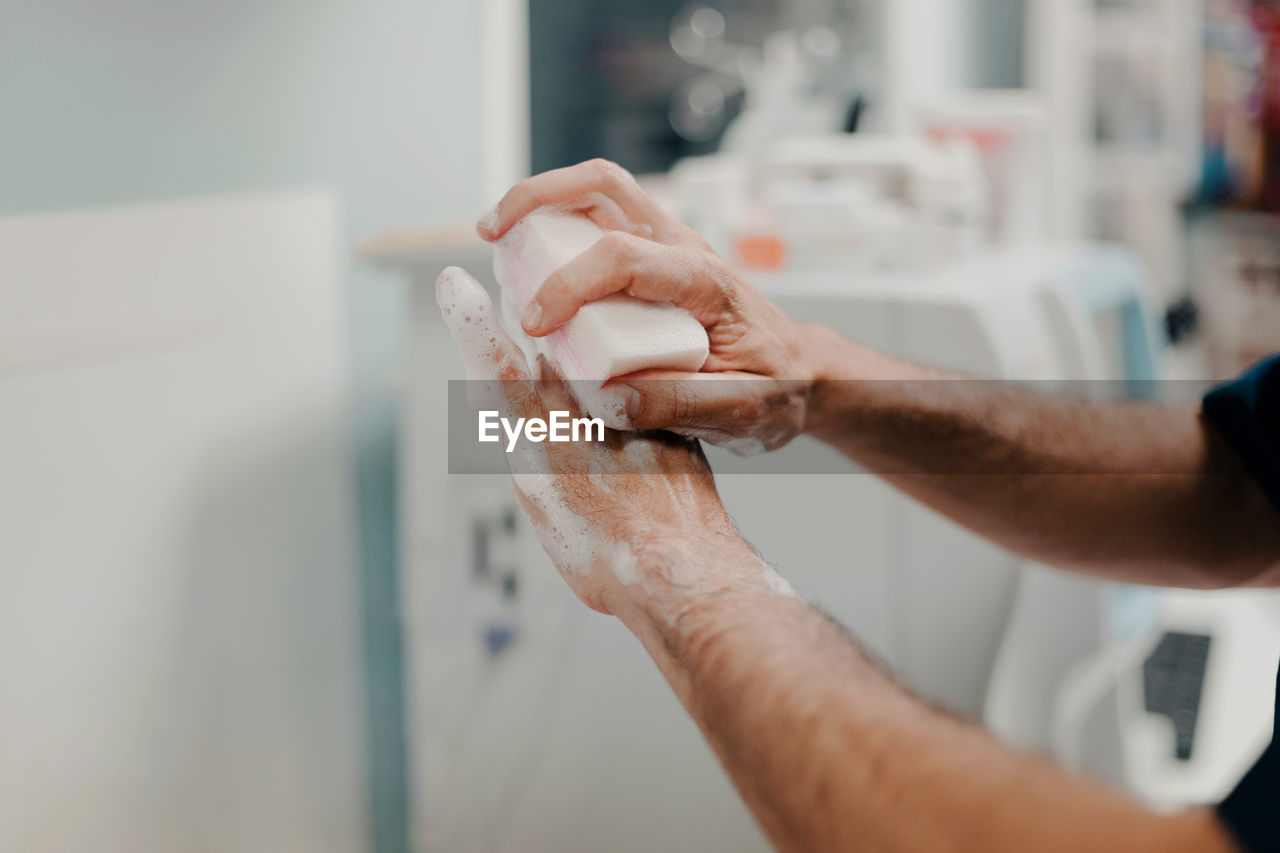 Crop side view of unrecognizable male doctor disinfecting hands in hospital