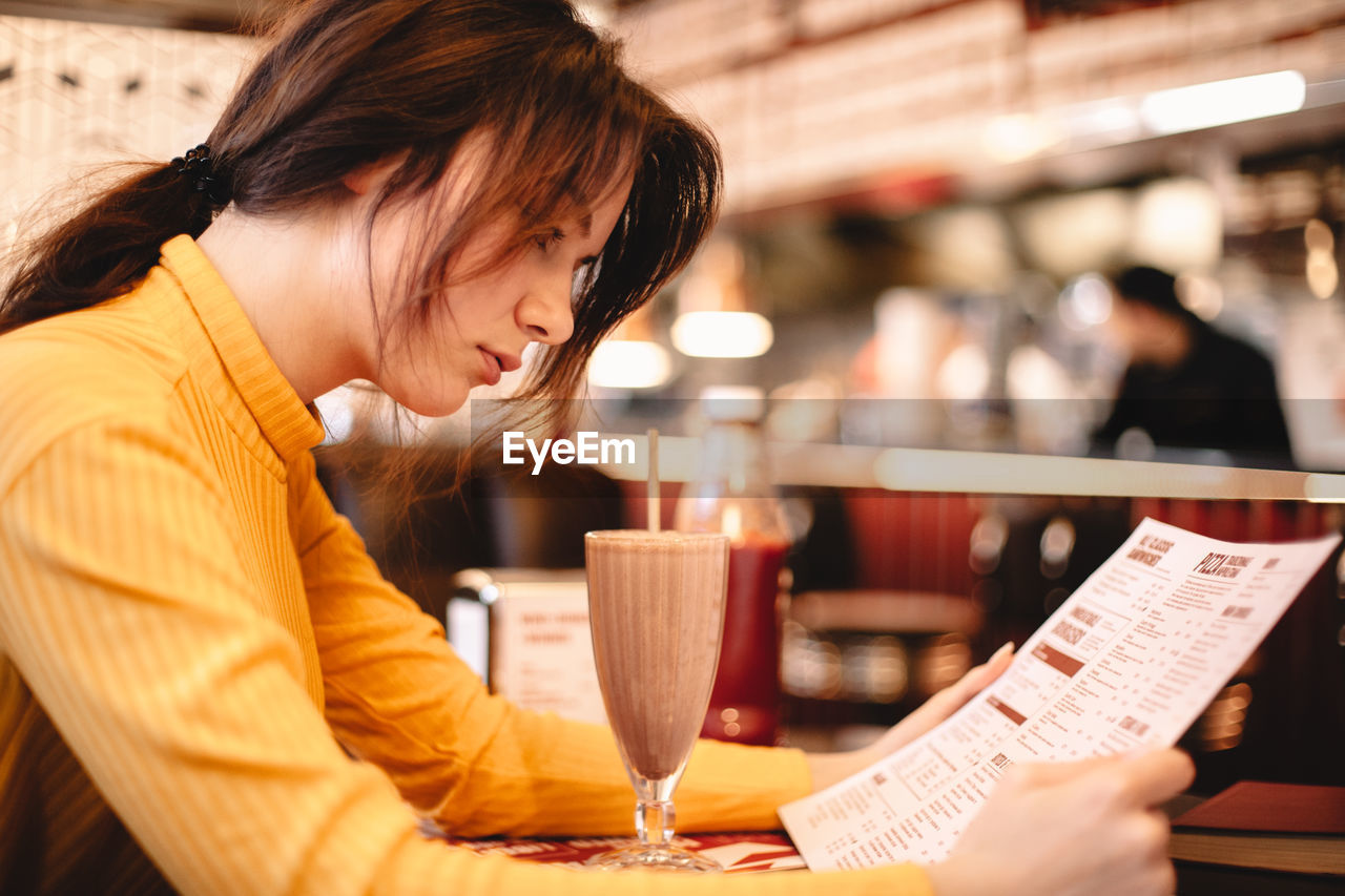 Teenage girl reading menu while sitting in restaurant