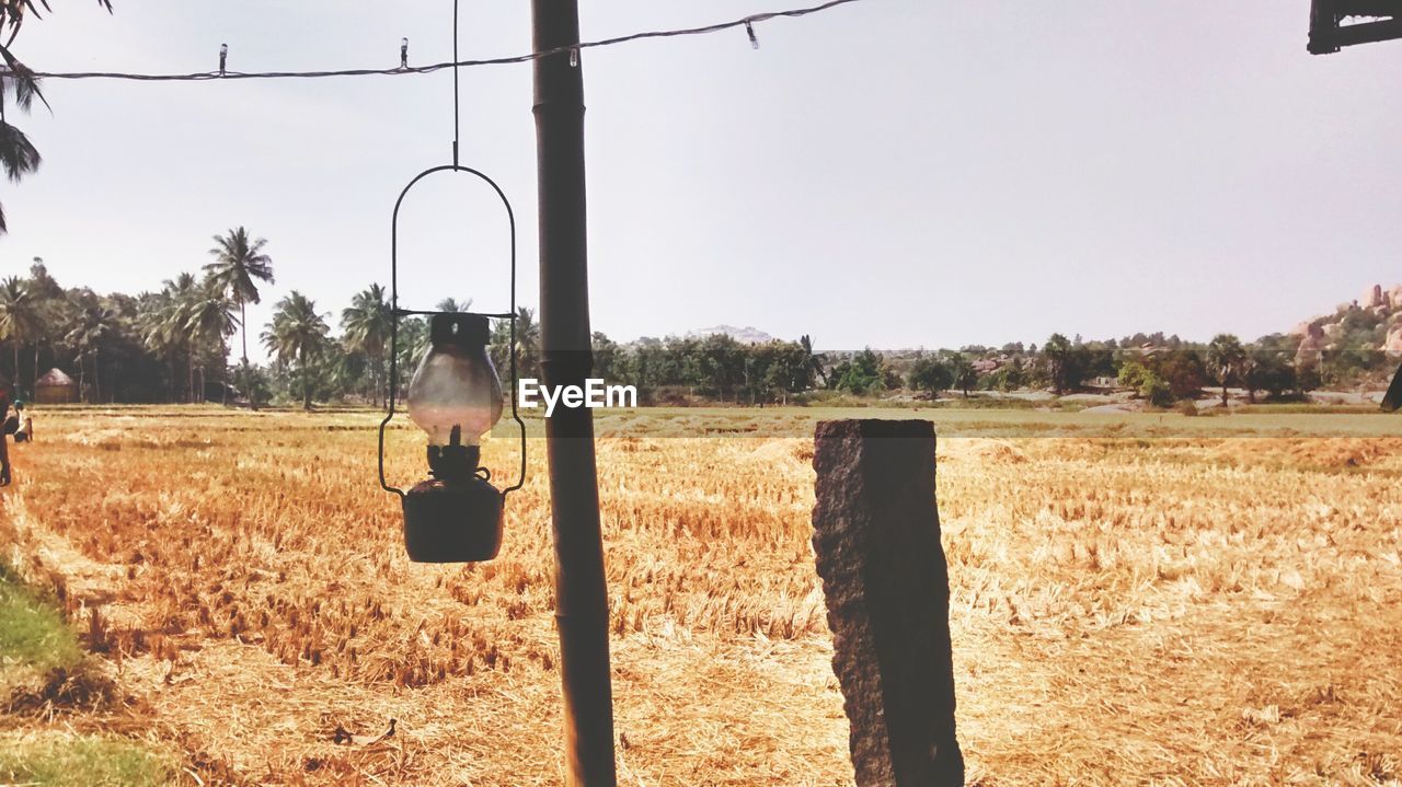 Old oil lantern hanging over agricultural field against clear sky