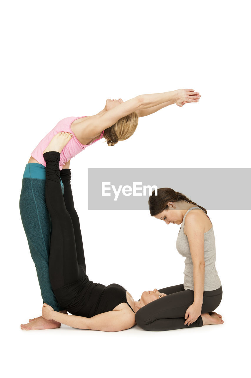 Side view of young women exercising against white background