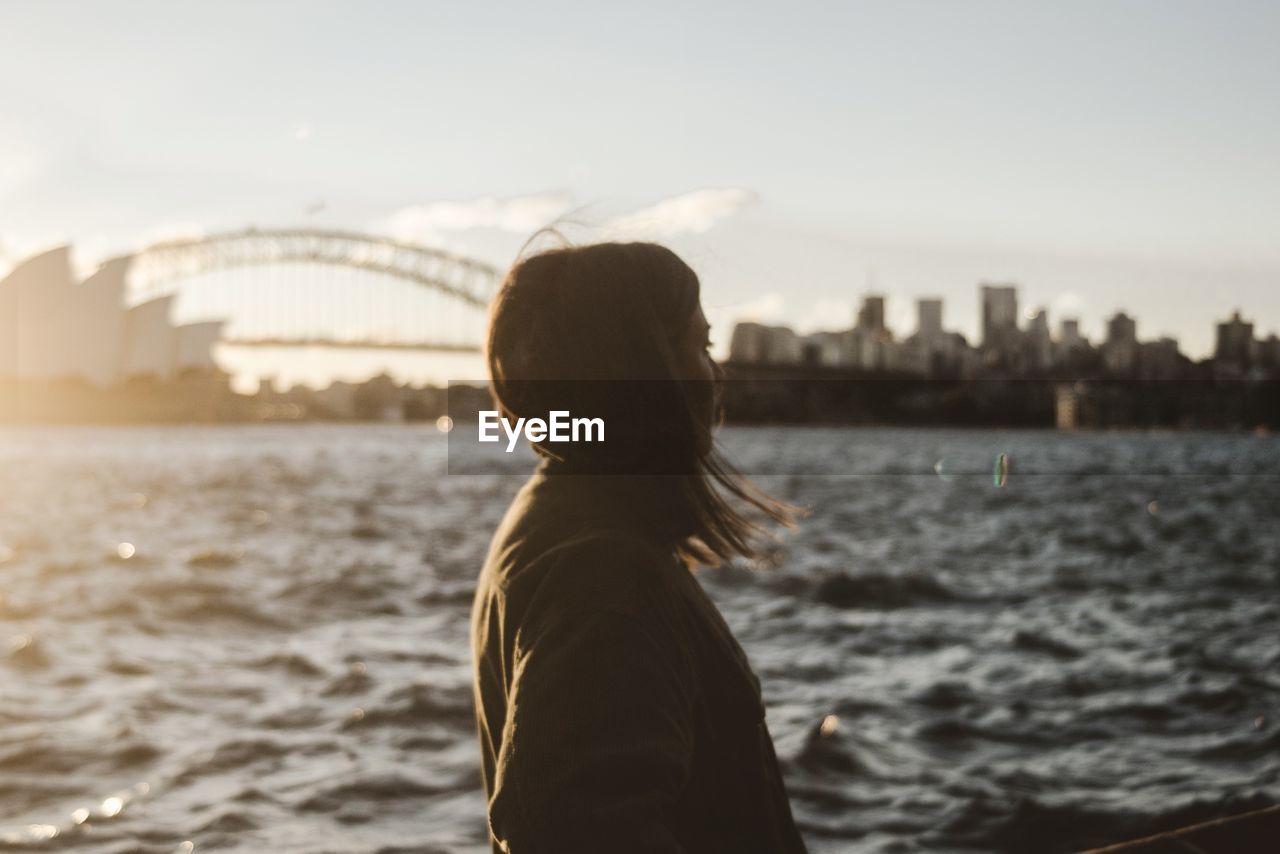 Side view of woman standing by river in city