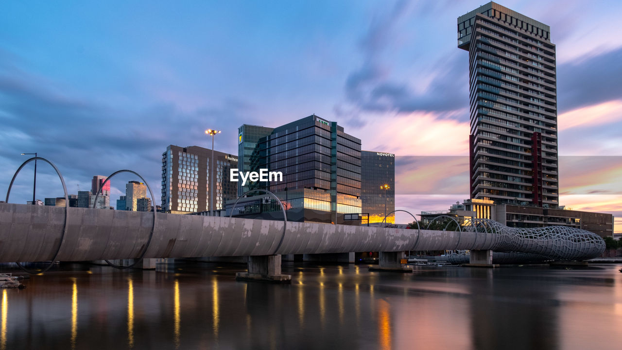 Reflection of buildings in city against sky during sunset