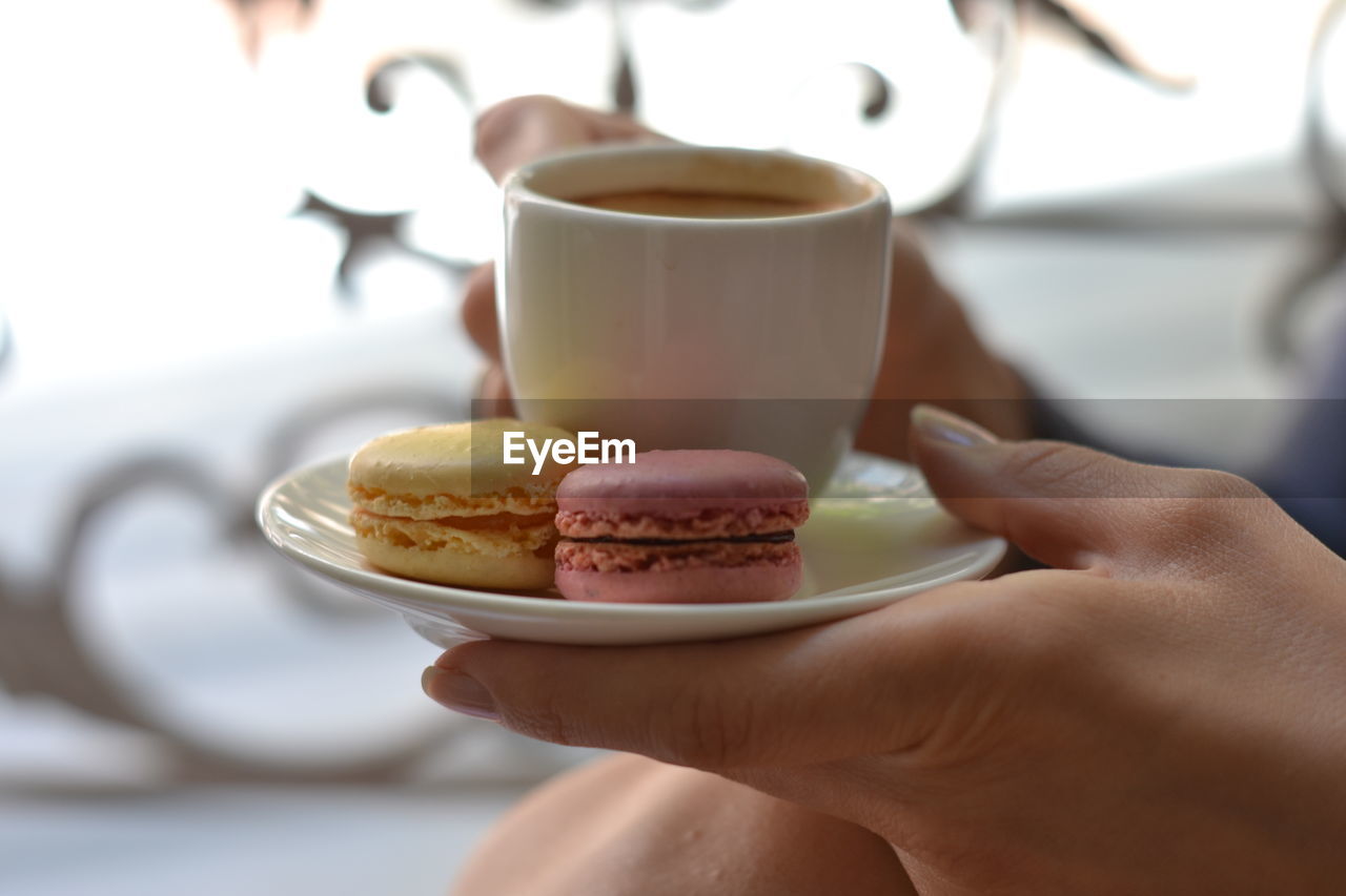 Cropped image of woman holding coffee cup with macaroons in saucer