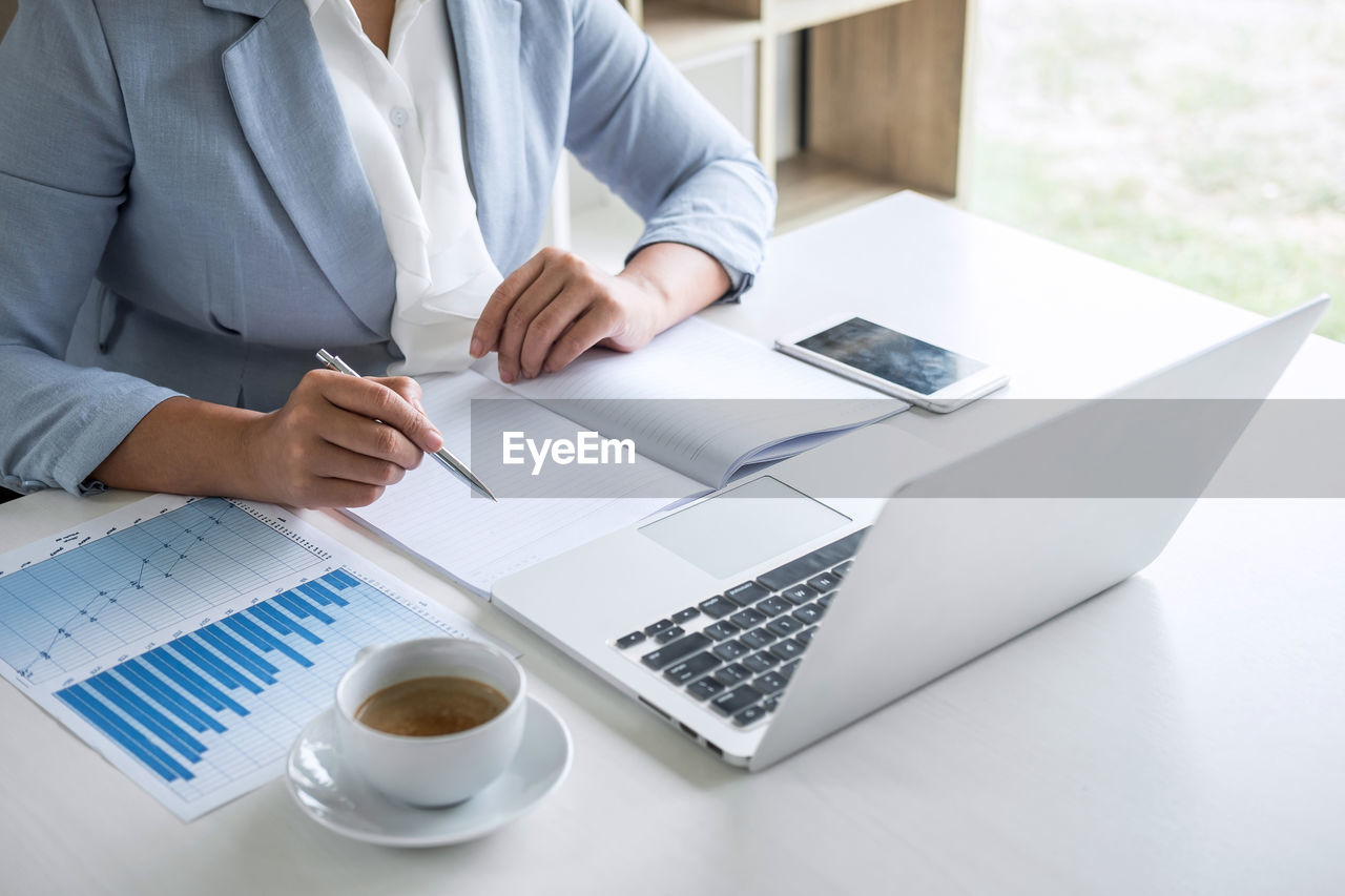 Midsection of businesswoman writing in book on table