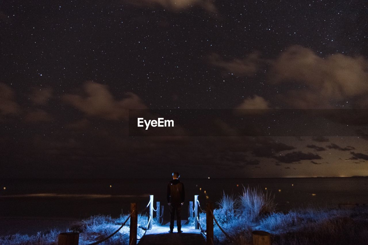 Rear view of man standing in boardwalk at night