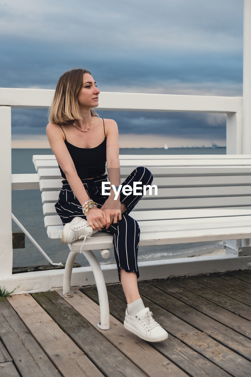 Young woman sitting on bench on wooden pier blurred beachside background. attractive female enjoying