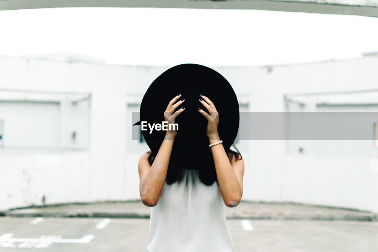 Woman standing on street and covering face with hat