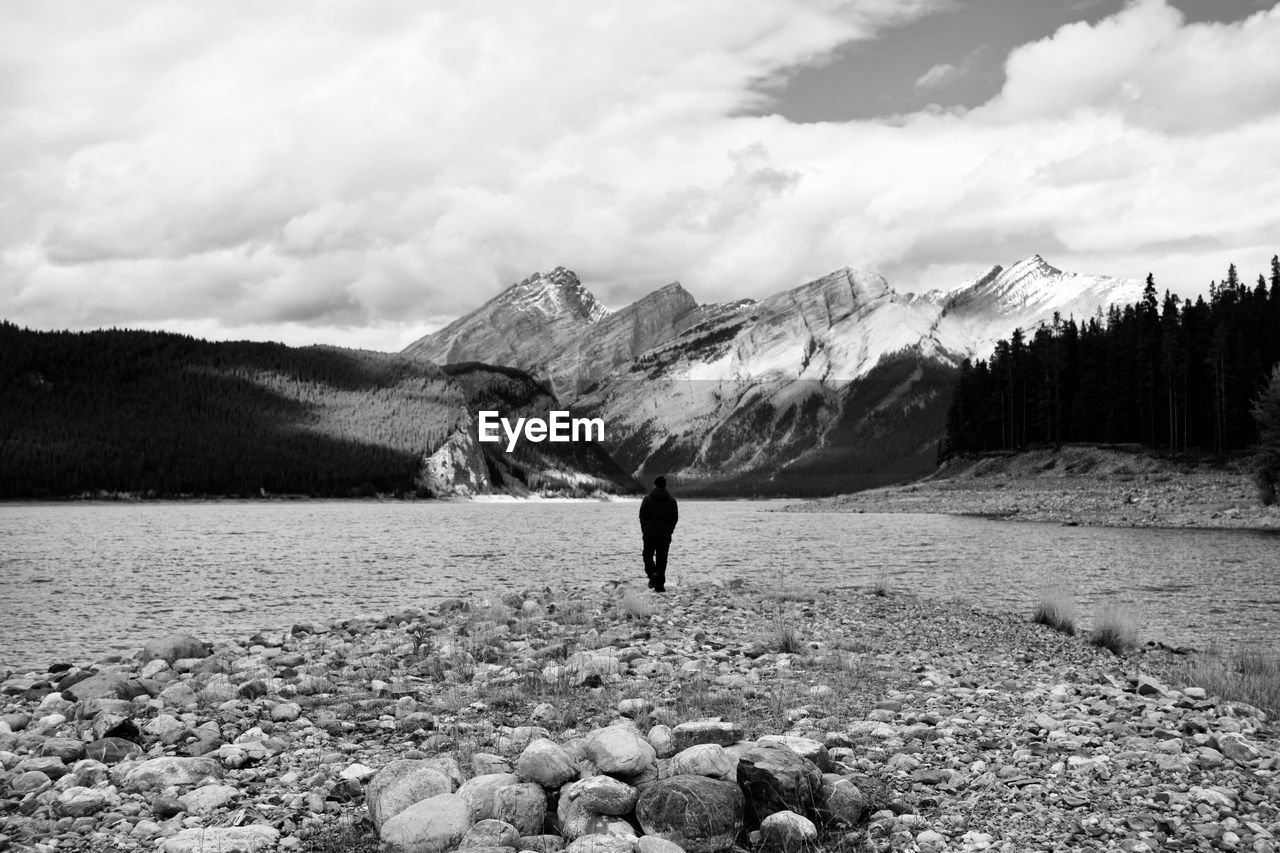 Rear view of man standing at lakeshore against sky