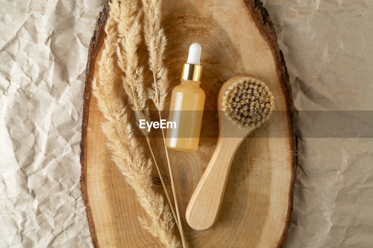 A dropper bottle of serum or oil with vitamin c and a face brush lying on a wooden tray