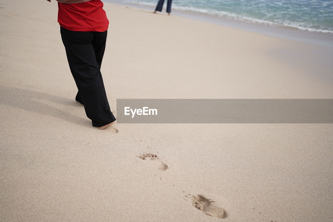 LOW SECTION OF MAN WALKING ON BEACH