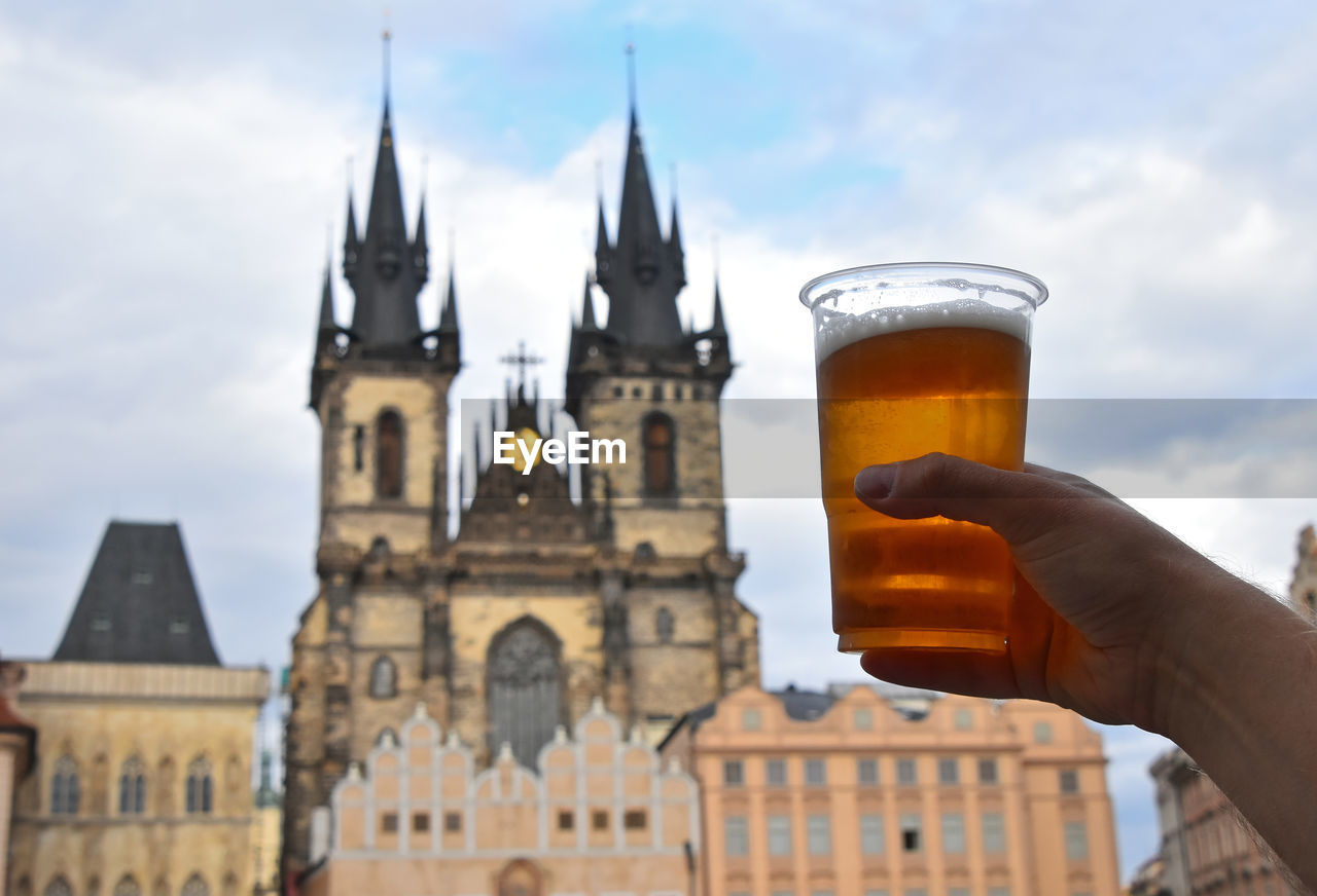 Cropped hand of man holding beer glass against cathedral