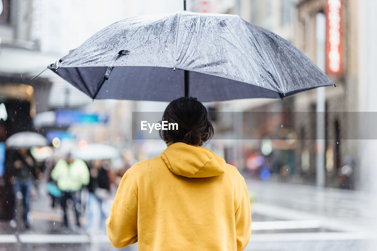 REAR VIEW OF WOMAN WITH UMBRELLA STANDING ON RAINY DAY