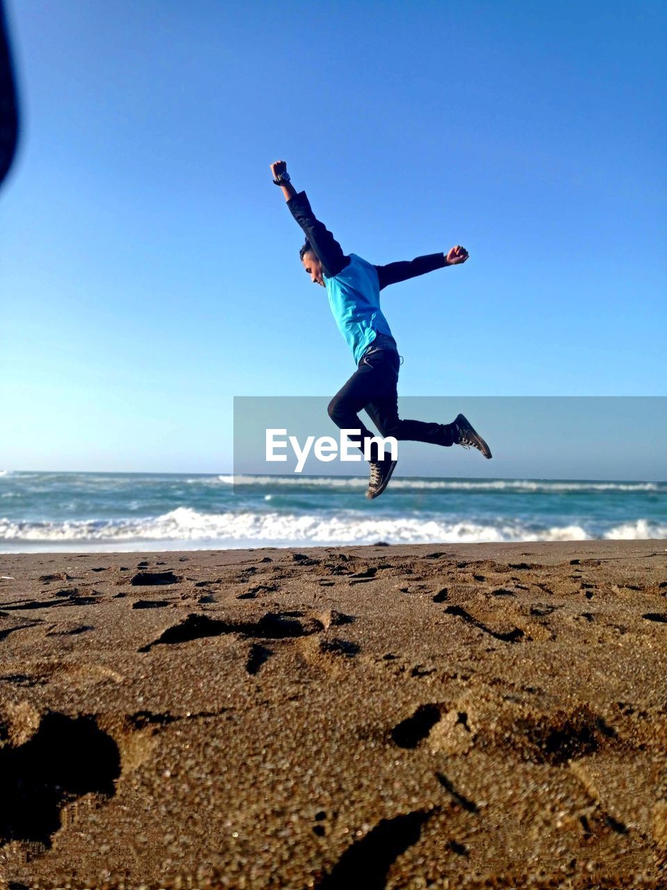 LOW ANGLE VIEW OF MAN JUMPING OVER SEA