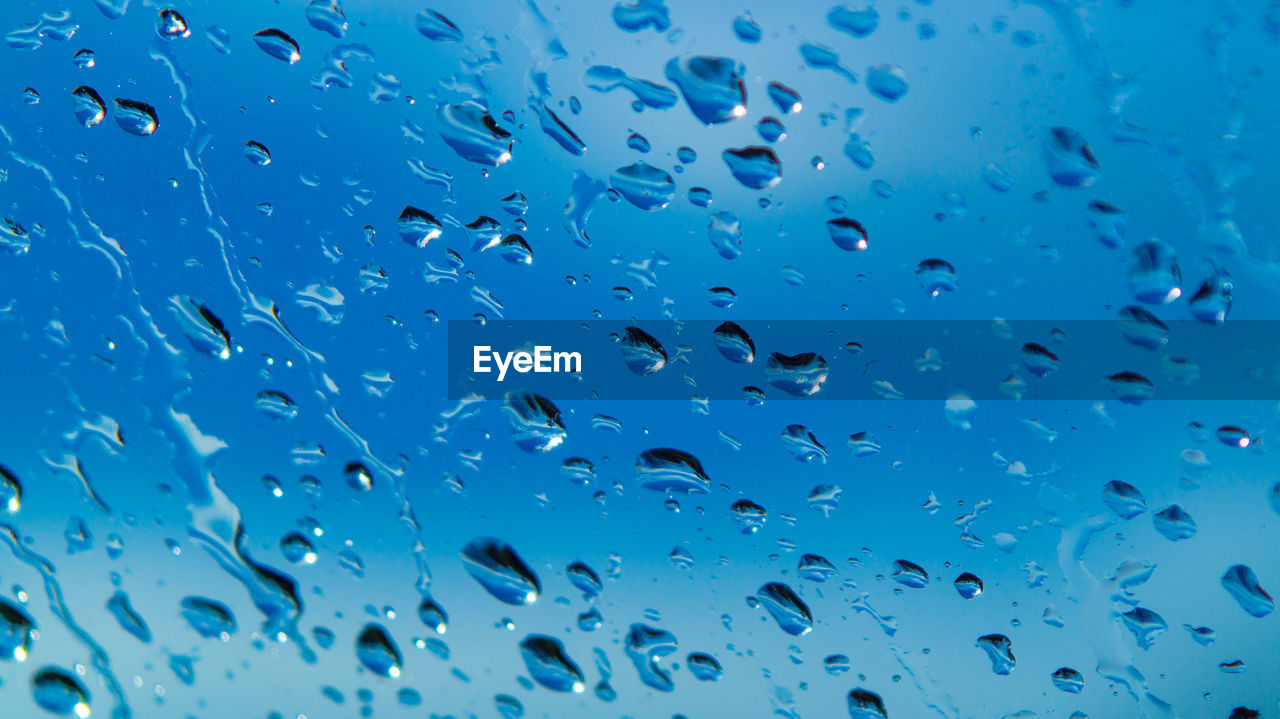 Full frame shot of wet glass window showing water droplets on sky background 