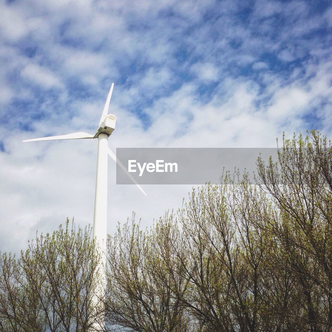 Low angle view of wind turbine against clouds